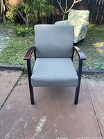 Side angle shot of the office chair outdoors, showing wooden armrest and grey upholstered seat and backrest.
