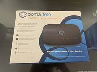 Front view of the sealed Ooma Telo box showing product name, image of device, and feature highlights like free nationwide calling and low international rates.