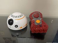 Photo showing the red and gray Thanos Infinity Gauntlet toy next to the white and orange Star Wars BB-8 toy on a reflective surface.