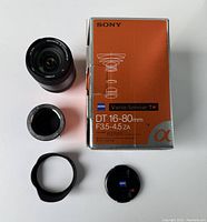 Top view of the Sony Alpha Vario-Sonnar lens, its lens hood, front and rear caps, and the original lens box with Sony and Zeiss branding, model details.