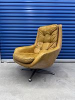 Front-side angle of vintage lounge chair showing tufted tan leather upholstery and metal swivel base.