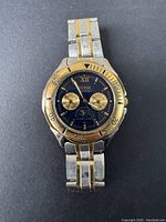 Top view of vintage Guess men's wristwatch showing gold and silver two-tone metal bracelet, black dial with two subdials, moon phase and date window.