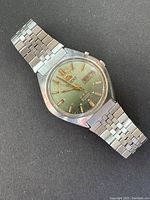 Front view of vintage Orient men's automatic watch showing green dial with gold-tone markers, day-date window, and stainless steel bracelet.