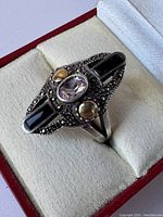 Close-up photo of the vintage ring showing details of the black onyx stones, marcasite accents, two small gold-tone spheres, and the central clear oval gemstone on the sterling silver base.