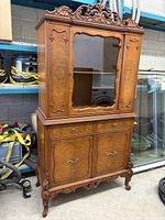 Front view of full hutch china cabinet showing upper glass display case, decorative carved crest, lower drawer and two cupboard doors.