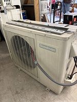 Outdoor condenser unit showing Goodman branding, ventilation grille, fan, and wiring.
