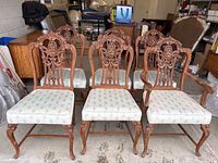 Front view of six chairs arranged in two rows showing carved backs and upholstered seats