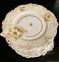 Stack of 12 antique Elysee Old Ivory IV dessert plates showing decorative floral and embossed pattern on plate rims.