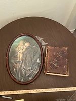 Wide view of the wooden oval framed portrait alongside an antique photo album showing wear.