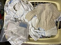 Basket with assorted vintage handmade baby clothes and linens including crocheted sweater and embroidered cloths.