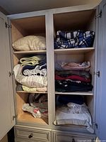 Photo showing the upper two shelves of the cabinet with folded quilts, afghans, blankets, and sheets in mixed colors and patterns.