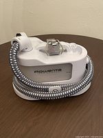 Front side view of the Rowenta clothing steamer showing brand name, water reservoir, hose and brush attachment.