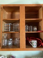 Image showing miscellaneous glass jars, glasses, bowls, and a ceramic mug inside a wooden cabinet with multiple shelves.