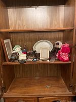 Curio cabinet shelf with assorted items including plush toy, doll, decorative plate, frames, small box, and other small items.