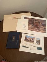 Overview of table with the Time Life First World War portfolio folder, blue hardcover book, and several prints including Nantucket photo and historical scene cards.