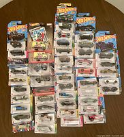 Top-down view of about 45 Hot Wheels cars and vehicles in packaging laid out on a wooden surface, showing the colorful variety and different themes.