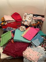 Wide view of assorted fabric pile with various colors and patterns including teal, burgundy, and pink fabric pieces and some animal prints visible