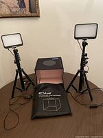 Lot contents showing two telescoping LED lights on adjustable tripods and Puluz foldable LED ring light studio cube on table.