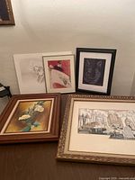 Five pieces of art, including a floral painting, cityscape drawing, wolf portrait, and two smaller unframed drawings leaning against a wall.