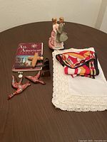 Lot contents displayed on a round dark wood table showing figurine, book, runner, scarf, and cross.