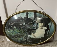 Full view of the oval metal framed print of a child sitting outdoors in a chair with garden scene and curved glass.