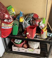 Photo showing black plastic two-tier storage shelf holding assorted lawn and garden supplies including Ortho Bug B Gon insect killer.