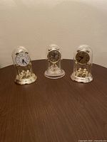 Image showing all three quartz anniversary clocks with glass domes in a row on a flat surface, highlighting size and style comparison.