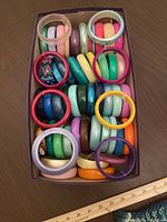 Top-down photo of a box containing various colorful vintage 1980s bangle bracelets, mostly chunky plastic.