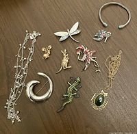 Top view of 10 various vintage brooches, pins, two necklaces and a bracelet arranged on a brown surface.