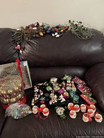 Multiple strings of colorful vintage Christmas lights laid out on a sofa along with various ornaments, mini mugs, and boxed sets of bulbs.