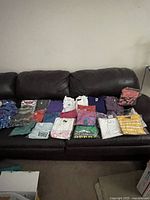 Wide view of 18 folded and bagged vintage shirts and sweatshirts laid out on a leather couch. Varied colors and styles, mostly sporty casual wear.