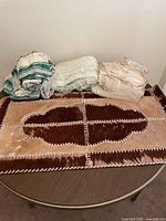 The cowhide rug folded with three sets of sheer kitchen curtains on top on a round table.