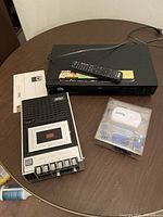 Photo showing Sony DVD/CD player with remote, Superscope portable cassette recorder, and boxed iPod speaker on wooden table