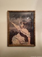 Full view of the hand embroidered needlework art showing a young girl pointing, framed behind glass with a decorative gold frame.