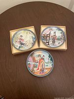 Three 1980s Japanese collector plates on brown table, two plates in beige original boxes, one plate outside box.