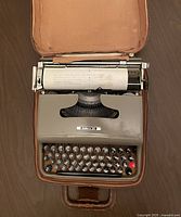Gray Olivetti Lettera 22 typewriter inside open brown leather carrying case, paper loaded with sample typed text.
