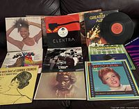 Multiple vinyl records from the 70s and 80s displayed laid out on a black surface. Includes visible covers and multiple album titles.