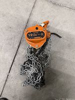 Orange 1/2 ton Jet KCH Series chain hoist with coiled steel chain on a concrete floor.