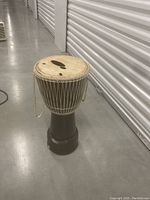 Photo of single wooden bongo drum standing upright with visible holes in the drumhead and rope tuning system intact.