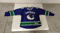 Photo of a blue Vancouver Canucks hockey jersey with green and white stripes and orca logo.