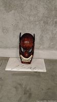 Front view of the dark red carved wooden mask showing facial details and condition.