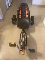 Front view of black Exit Rocket Fire trike with flame decals on seat and visible pedals and tires.