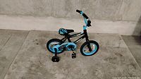 Photo of a kids' bike with black and blue color scheme, showing training wheels, pedals, handlebars, and seat.