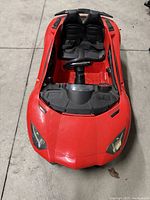 Front view of red Lamborghini-style kids electric ride-on car showing two seats with seat belts, steering wheel, and realistic hood detailing.