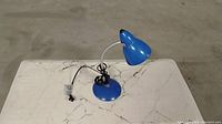 Photo of a single blue adjustable desk lamp with clamp base on a white surface.