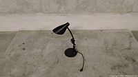 Black adjustable desk lamp with conical shade and round base on grey surface