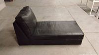 Side view of black faux leather lounger showing cushioned backrest and seat.