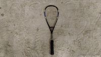 Photo of a black and grey Wilson tennis racket lying on a beige carpet