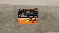 Photo of original box containing two Ridgid cordless power tools, a drill and an impact driver, on carpeted floor