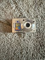 Front view of Sony Cyber-shot camera placed on carpet, showing lens, brand name, and feature stickers.